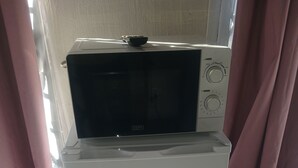 A white refrigerator with a microwave on top, a white trash bin, and pink curtains in a room with tiled flooring.