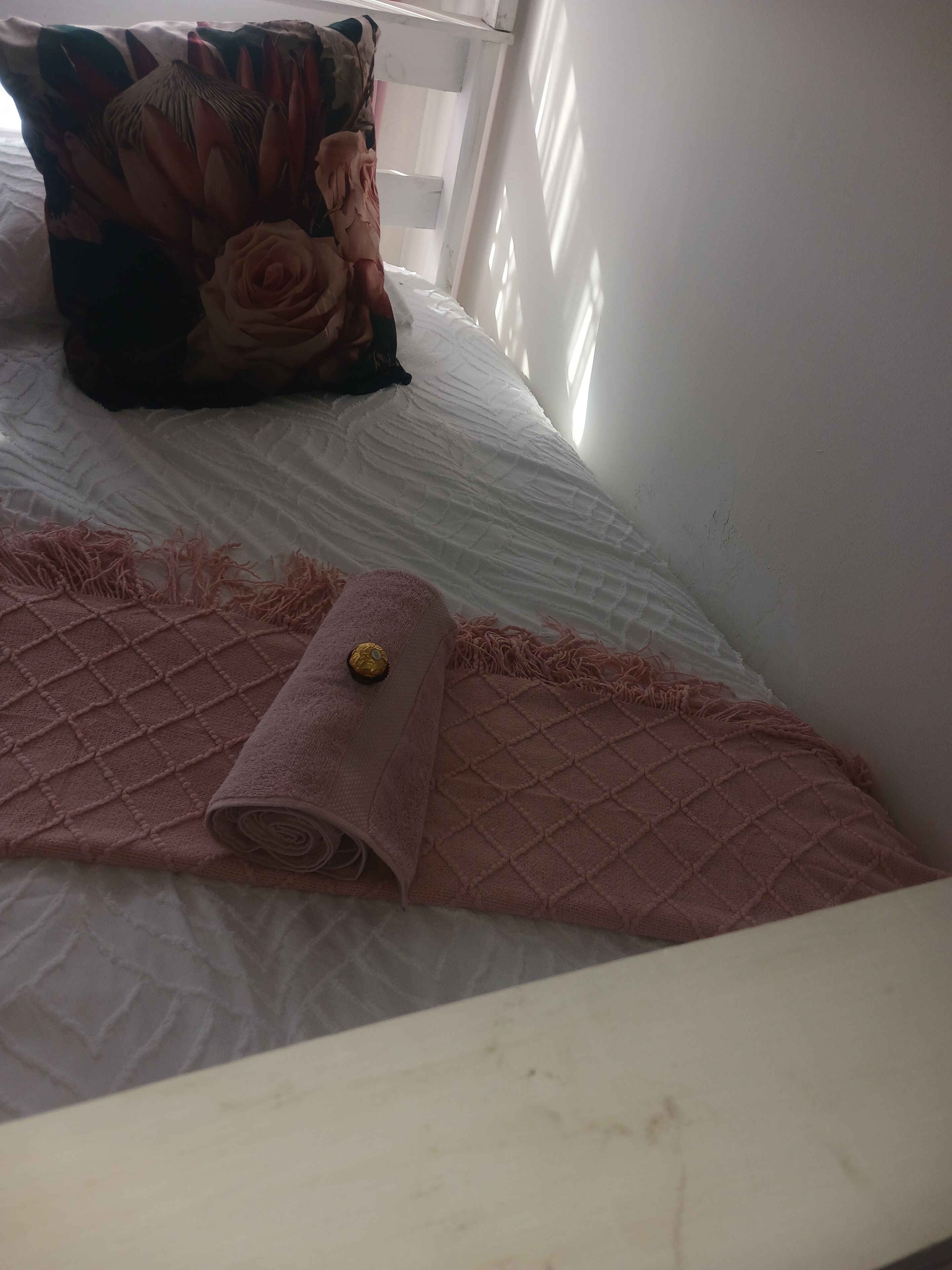 A bed with a white mattress, a pink quilted blanket, and a rolled-up towel.
