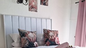A neatly made bed with a white duvet, pink and floral pillows, and a pink throw blanket.