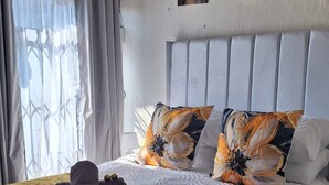 A hotel room with a large bed, a headboard, a window with curtains, and a wall-mounted air conditioner. - Room-tranquil Guest Room in Randburg wit (Johannesburg)