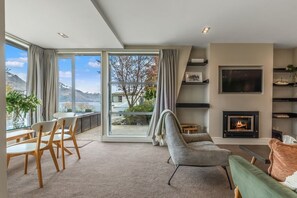 Ein modernes Wohnzimmer mit Kamin, großen Fenstern und Blick auf See und Berge.