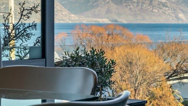 A room with a large window offering a view of snow-capped mountains and a body of water. - Adelaide Courtyard | Walk to Town - Free Parking (Queenstown)
