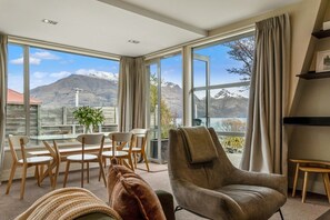 A modern living room with a large window, a dining area, and a cozy seating area. - Adelaide Courtyard | Walk to Town - Free Parking (Queenstown)