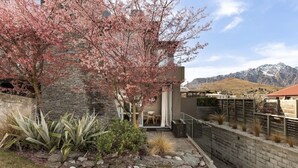 A modern house with a stone wall, a cherry blossom tree, and a view of mountains. - Adelaide Courtyard | Walk to Town - Free Parking (Queenstown)