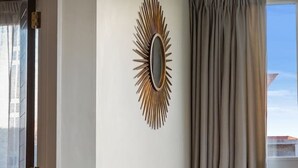 A modern living room with a sofa, a dining table with chairs, a decorative mirror, and a view of the city through large windows. - Adelaide Courtyard | Walk to Town - Free Parking (Queenstown)
