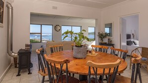 A round wooden table with chairs, a potted plant, and a clock on the wall. - Rustic 3 Bedroom Beach Cottage, perfect for a peaceful getaway. (Birkenhead, Gansbaai)