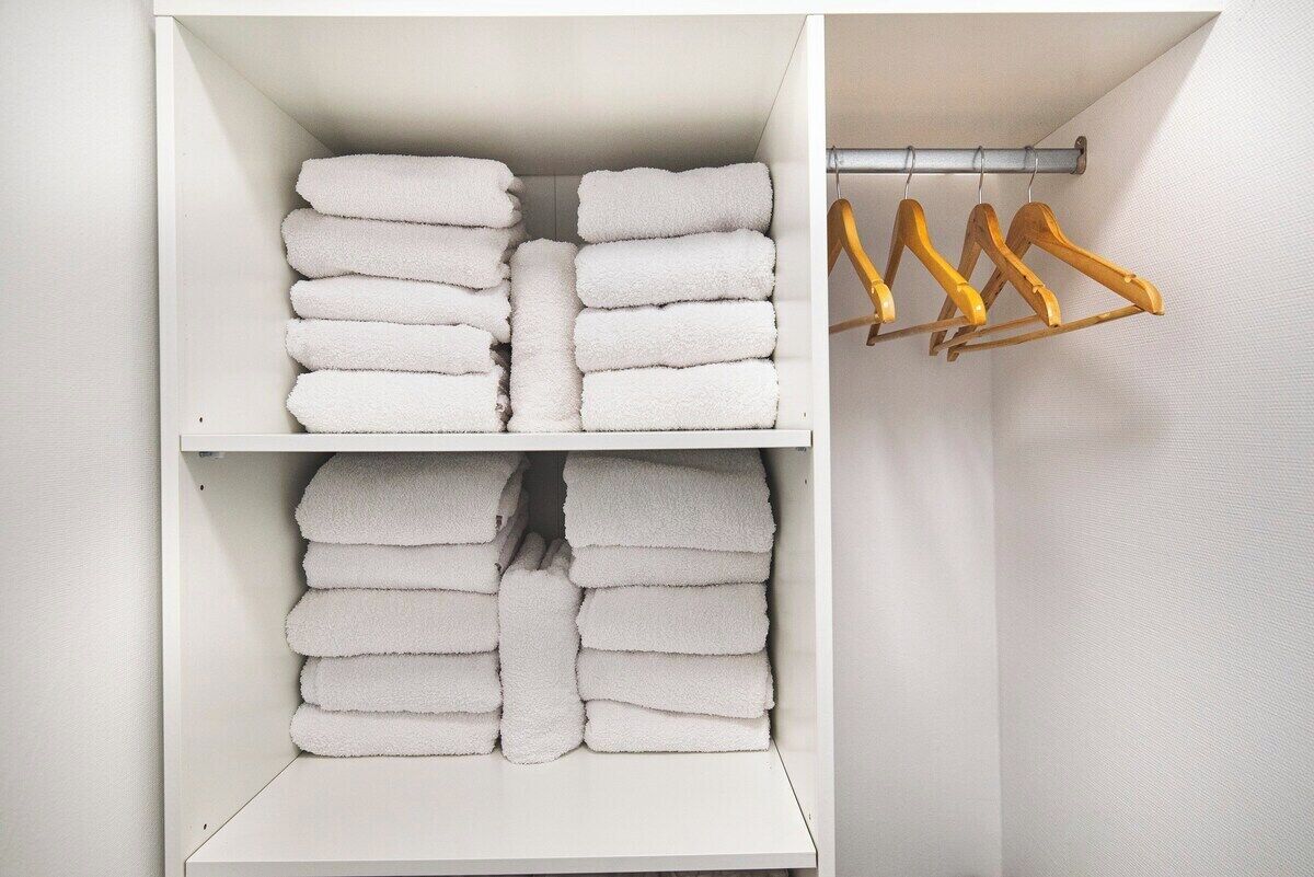 A white storage unit with multiple shelves holding neatly folded white towels.