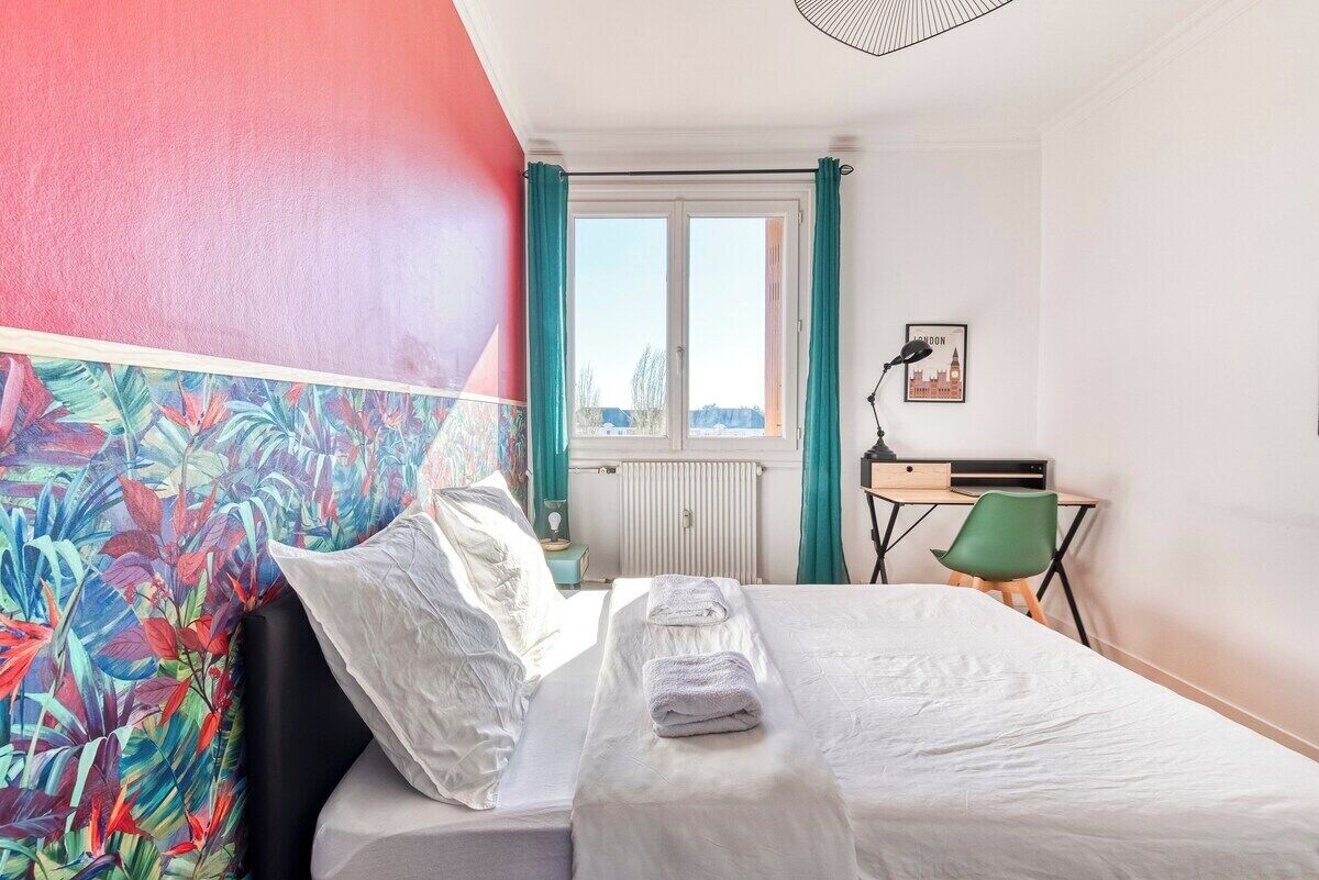 A hotel room with a bed, a desk, a chair, a window with curtains, and a cityscape view.