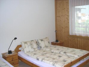 Ein Schlafzimmer mit einem hölzernen Bett, einem Nachttisch, einer Lampe und einem Fenster mit Vorhängen.