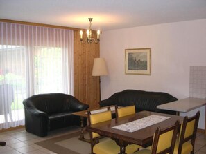 Ein Essbereich mit einem Holztisch, vier Stühlen, einer schwarzen Ledersofa, einer Lampe und einem gerahmten Bild an der Wand.