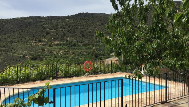 Una piscina amb una tanca de metall negre, envoltada de vegetació i turons al fons.