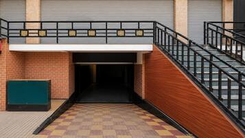 Ein Gebäudeeingang mit einer Ziegelwand, einem Metallgitter und einer Treppe mit schwarzem Geländer.