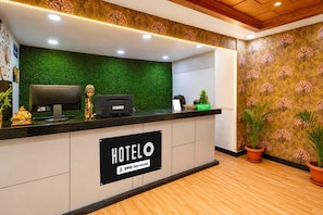 A hotel reception desk with a green wall, a sign indicating it is serviced by OYO, and a reception area with a wooden floor.