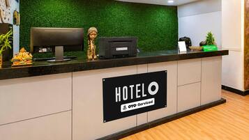 Balcão de recepção de hotel com parede verde, placa de recepção, computador e impressora.