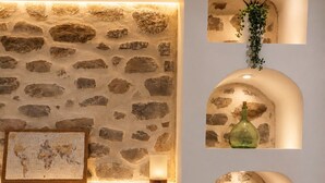 Ein Schlafzimmer mit Steinsandsteinwand, einem Bett mit beigefarbener Bettwäsche und drei beleuchteten Regalen mit diversen Gegenständen.