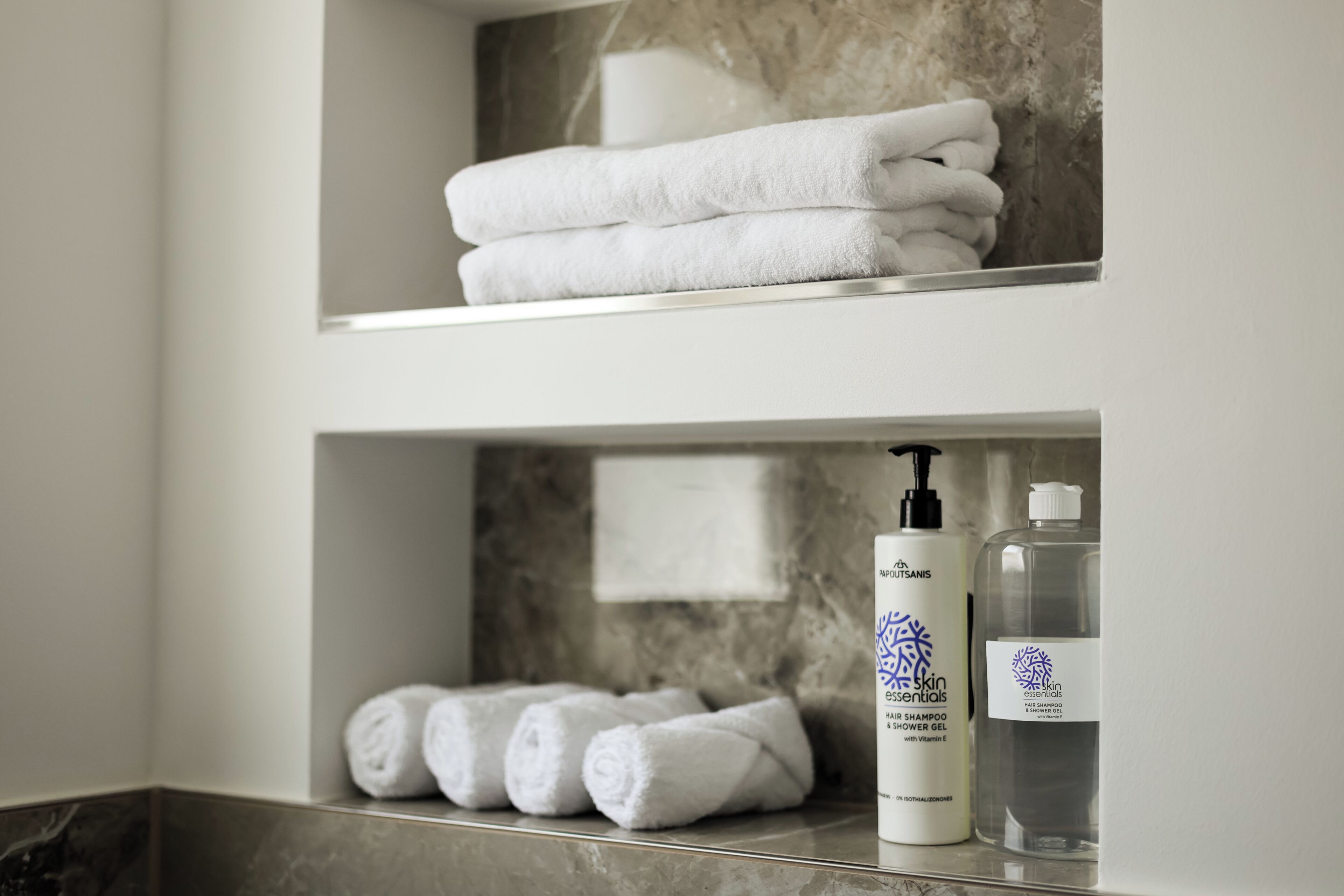 A bathroom with a marble wall, a shelf with folded towels, and two bottles of shampoo.