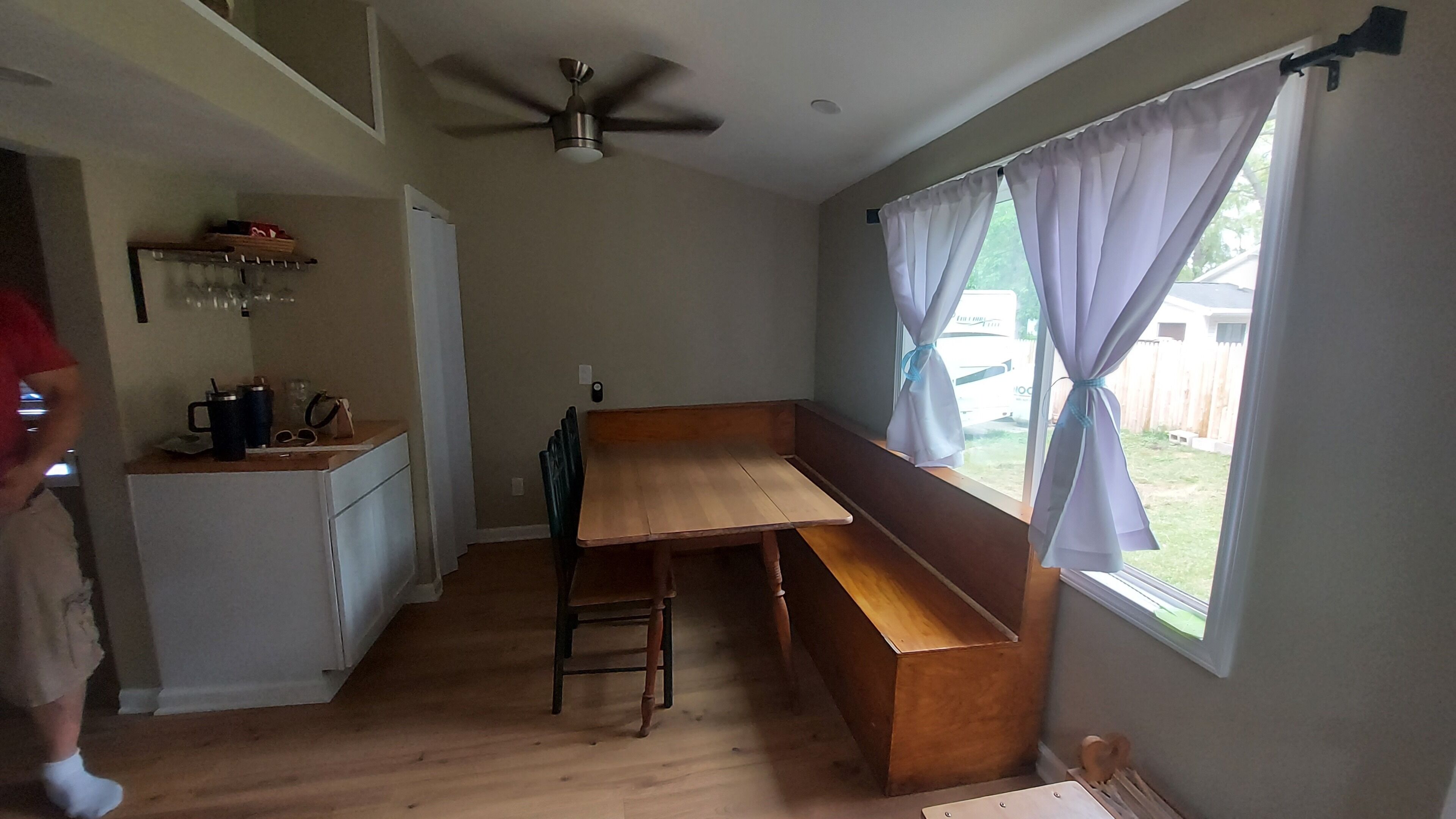 Une cuisine avec un banc en bois, un ventilateur de plafond et une fenêtre avec des rideaux.