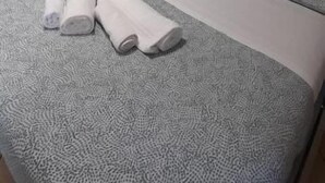 Ein Schlafzimmer mit einem Bett, einem Nachttisch, einer Lampe, einem Kleiderschrank und einem kleinen Hocker.