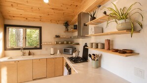 A modern kitchen with wooden cabinets, a gas stove, a microwave, and various kitchen utensils. - Scandinavian Cabin on Sandy Lakefront [NEW RENOVATION] (Lake Ann)