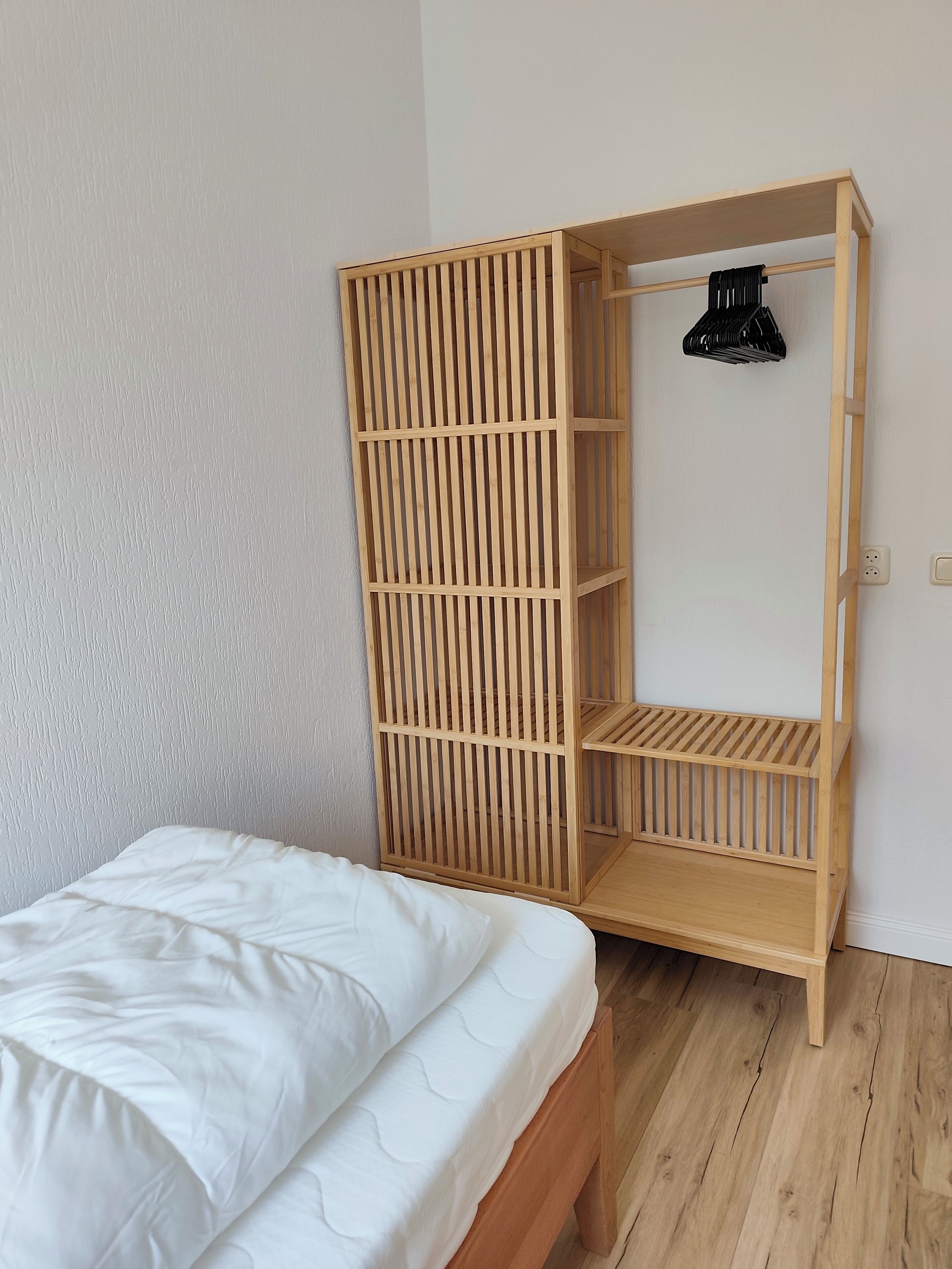 Une armoire en bois avec plusieurs étagères et une tringle pour suspendre les vêtements, un lit avec une literie blanche et un plancher en bois.