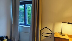 Een kamer met een bed, nachtkastje met lamp, raam met gordijnen en een radiator.