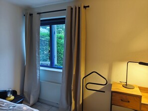 A room with a bed, a bedside table with a lamp, a window with curtains, and a radiator. - Cozy vacation home near the water—a relaxing getaway for people and their dog(s)! (Julianadorp)