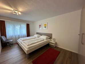 Ein modernes Schlafzimmer mit einem Doppelbett, einem Nachttisch, einem Sessel und einem roten Teppich.