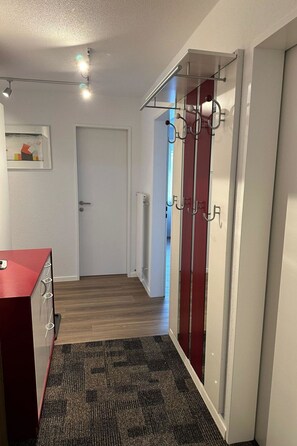 Ein Flur mit Holzboden, einem roten Schrank, einer Tür mit Kleiderhaken und einem gerahmten Bild an der Wand.