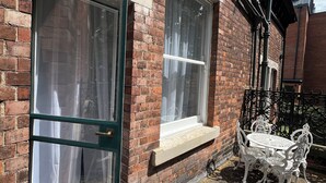A brick building with two windows, one open, and a small outdoor seating area with a table and chairs. - O Romeo Suite at Elmwood House (Nottingham)
