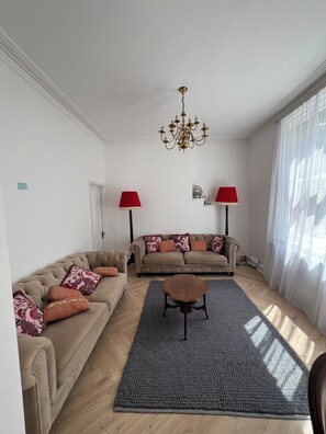 A living room with two sofas, a coffee table, a chandelier, and a large window with sheer curtains. - O Romeo Suite at Elmwood House (Nottingham)