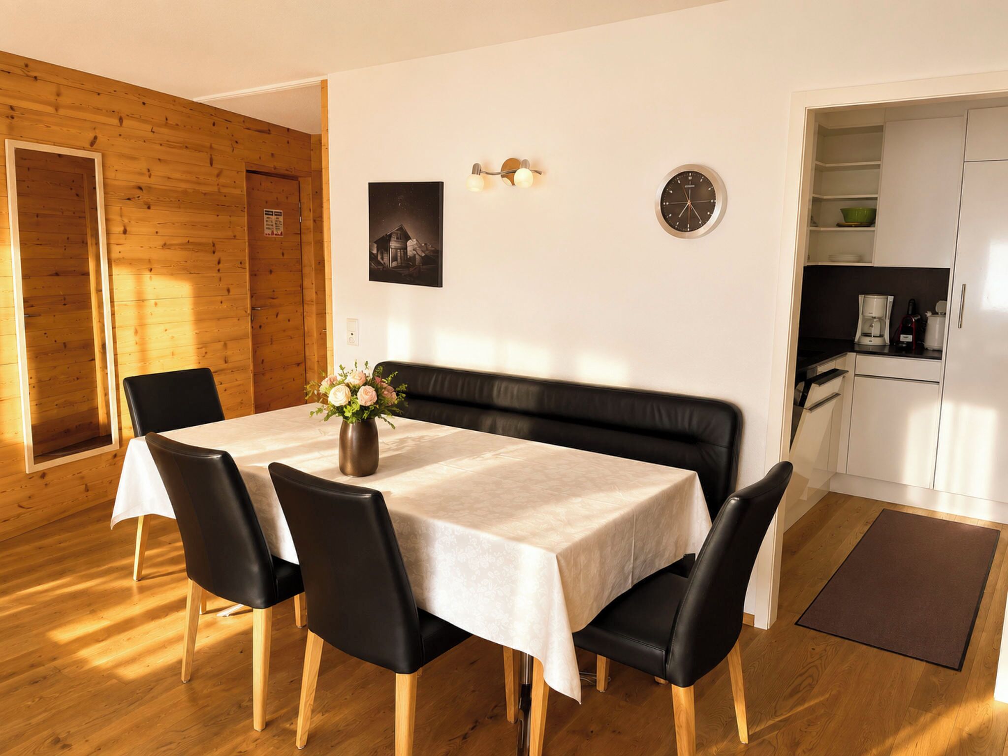 A dining area with a table set for four, a bench, and a clock on the wall.