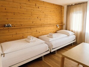 Ein Zimmer mit zwei Einzelbetten, Holzwandverkleidung, einer kleinen Ablagefläche mit Dekoration und einem Fenster mit Vorhängen.