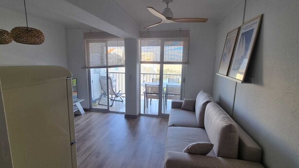 A spacious living area with a sofa, a ceiling fan, and a view through large windows. - Charming apartment near the beach (Empuriabrava)