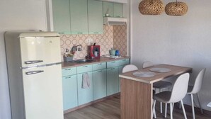 A compact kitchen with a refrigerator, a sink, and a dining area with chairs and a table. - Charming apartment near the beach (Empuriabrava)