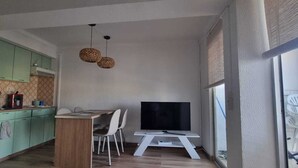A compact kitchen with green cabinets, a dining table with chairs, a flat-screen TV, and a large window. - Charming apartment near the beach (Empuriabrava)