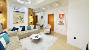 A modern living room with a sofa, armchairs, a coffee table, and artwork on the walls. - Beautifully Styled 2 Bedroom Apartment in Salem Ikate. QQ (Ikate)