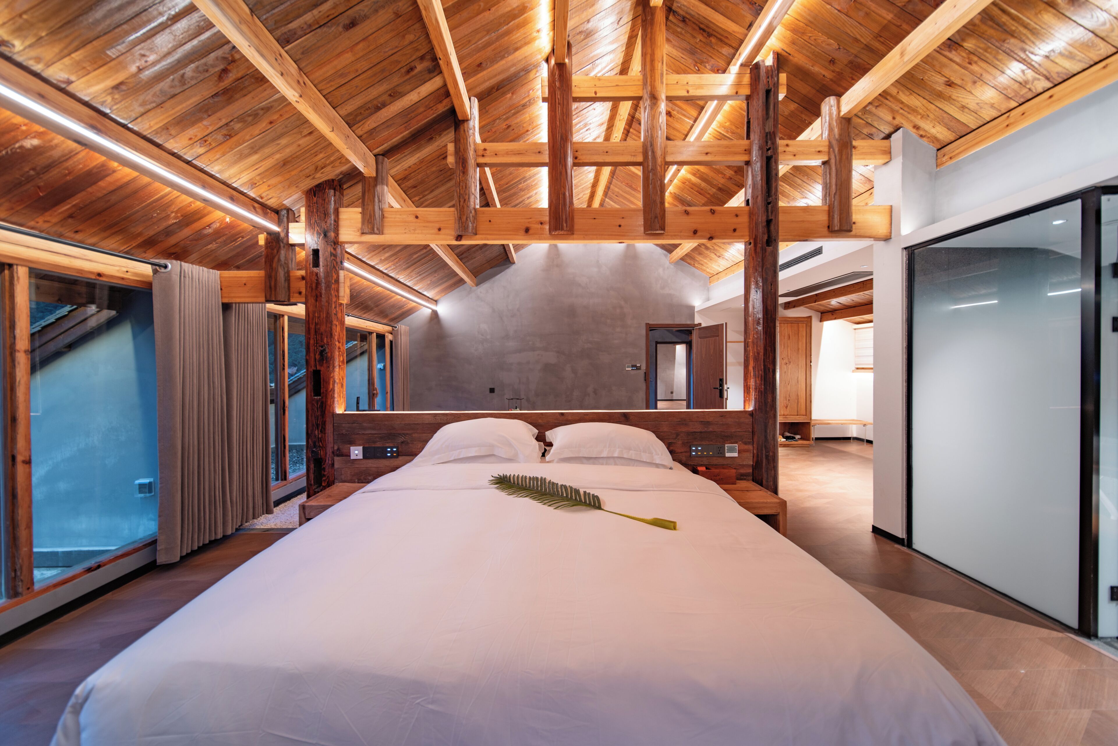 Una cama grande con decoración de hojas, vigas de madera y vistas al exterior.