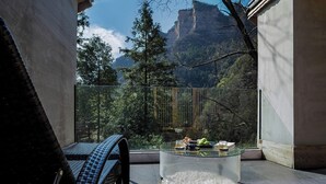Een balkon met een glazen tafel, rieten stoelen en uitzicht op een berg.