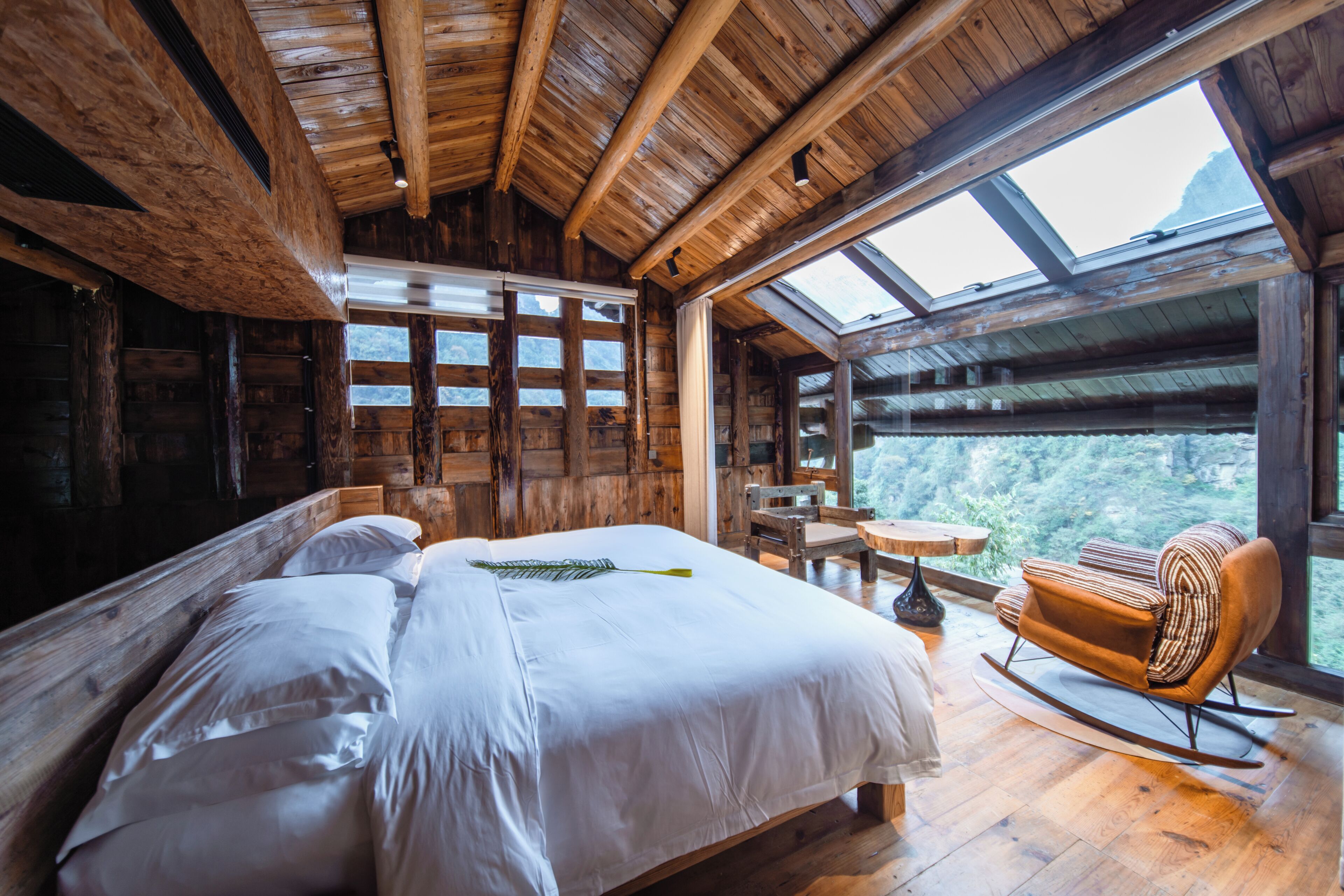 Una habitación de cabaña de madera con una cama grande, una mecedora, una mesita y vistas a través de un tragaluz.