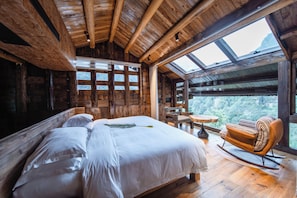 Una habitación de cabaña de madera con una cama grande, una mecedora, una mesita y vistas a través de un tragaluz.