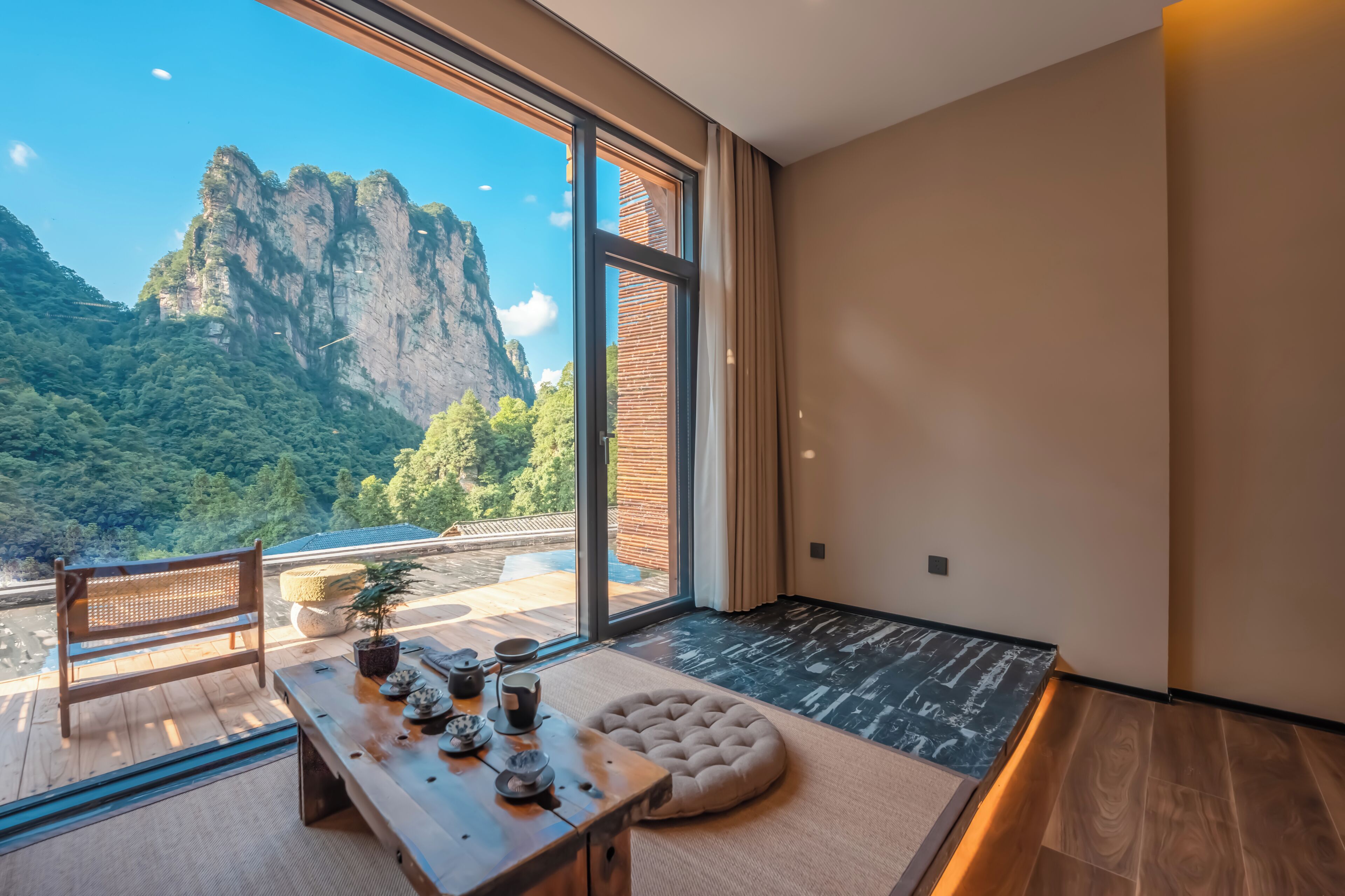 Una habitación con un ventanal grande, una mesa de madera con juego de té, un asiento acolchado y vistas a la montaña.