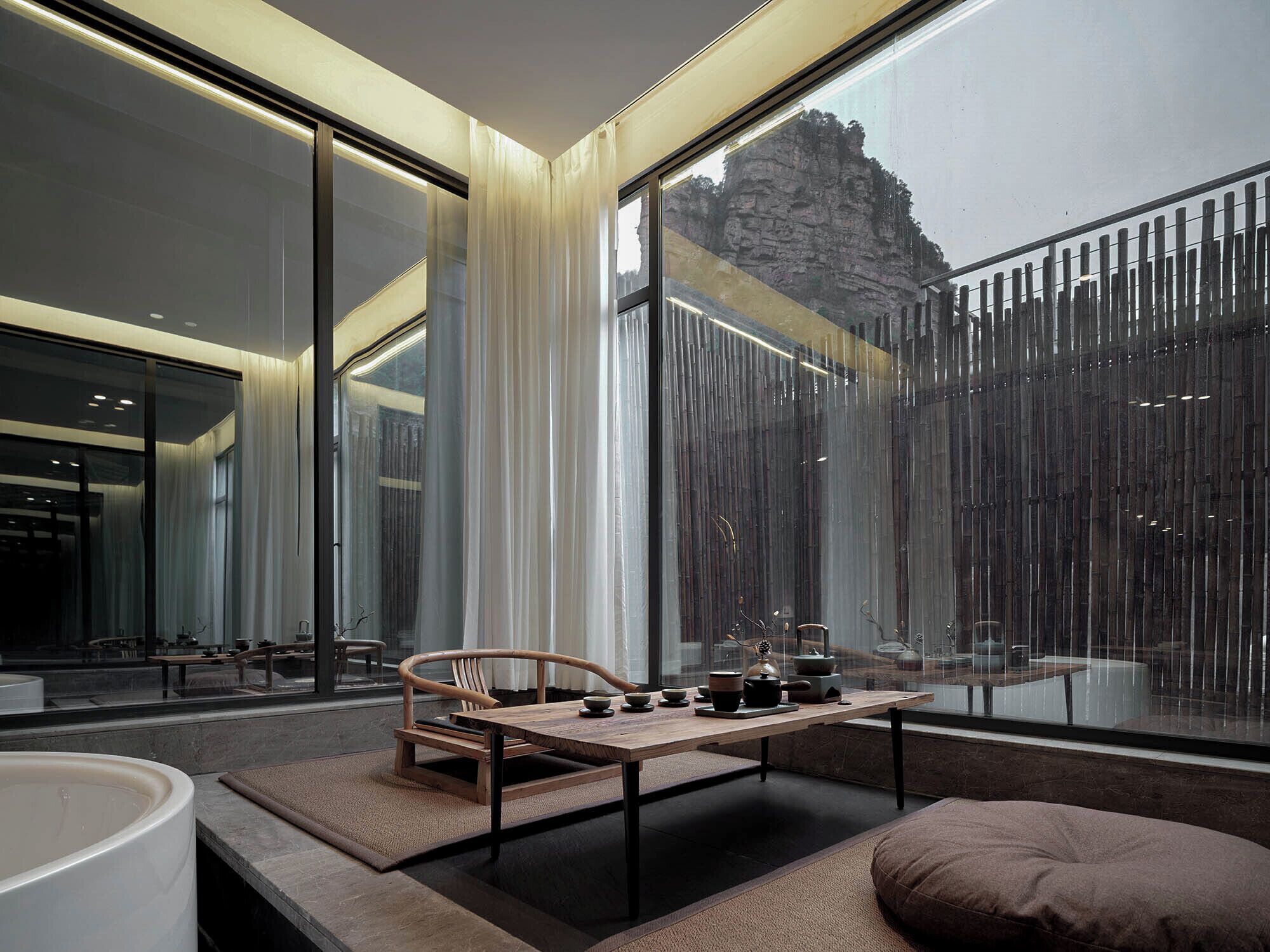 A modern interior with large windows, a wooden table with tea set, and a cushioned seating area.