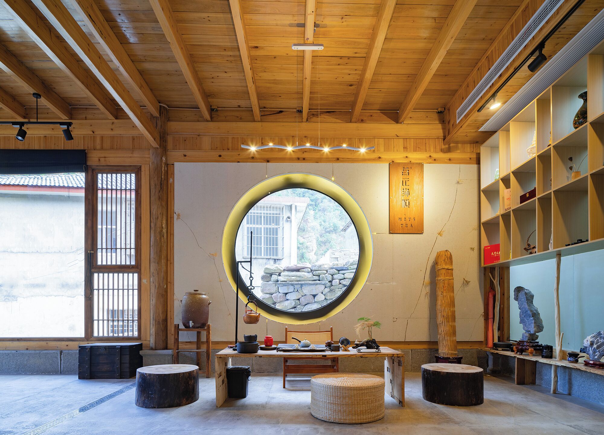 Un interno tradizionale con travi in legno, una finestra rotonda, tatami, un set da tè e un muro in pietra.