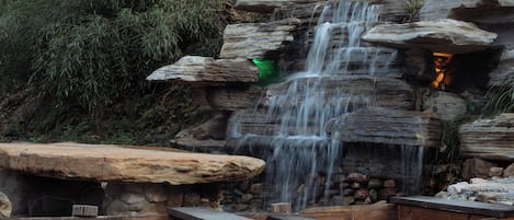 A waterfall cascading over rocks, wooden benches, and a stone wall.