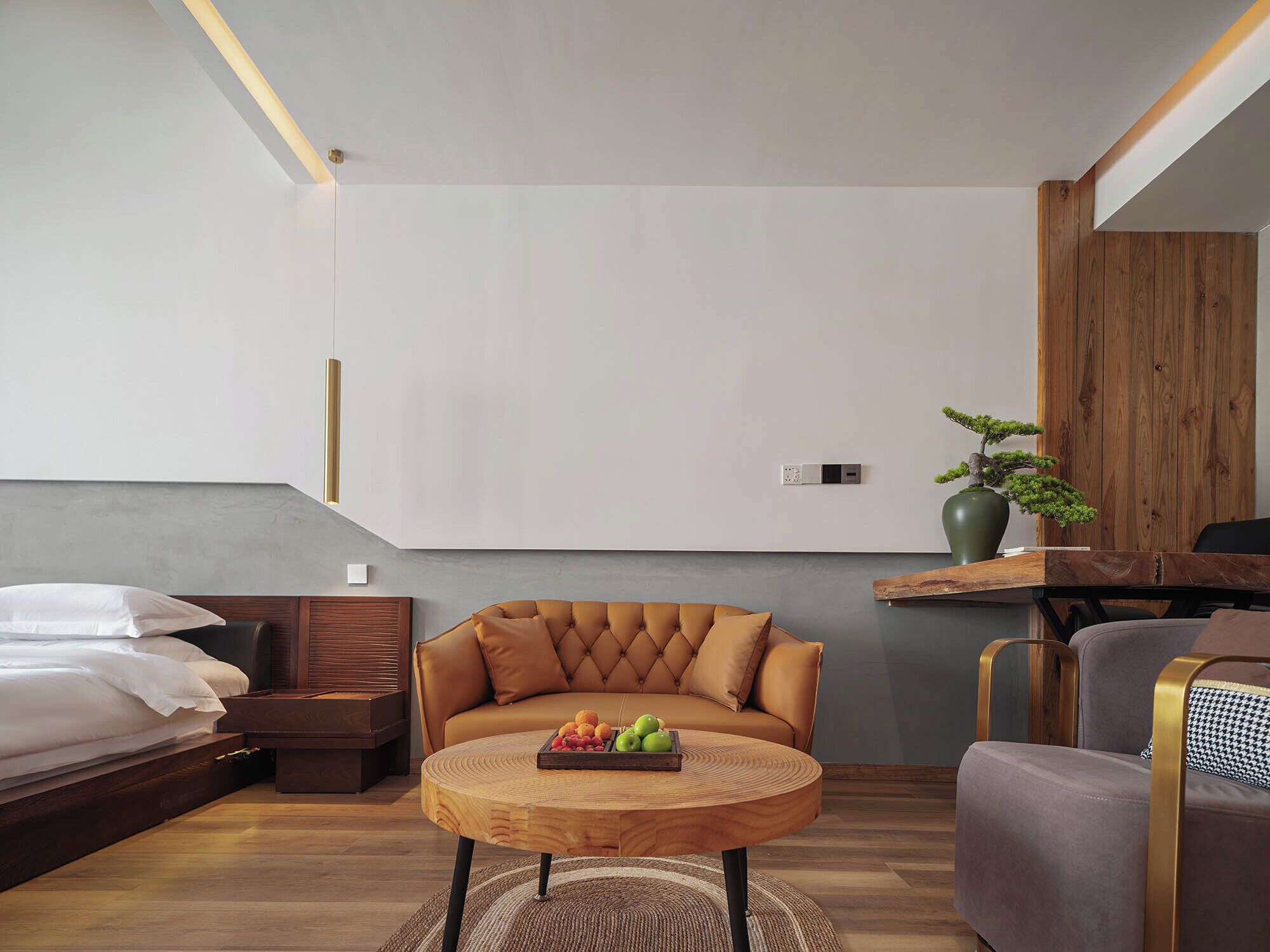 Un dormitorio moderno con cama, sofá, una mesa redonda de madera con fruta y un bonsái.
