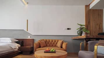Un dormitorio moderno con cama, sofá, una mesa redonda de madera con fruta y un bonsái.