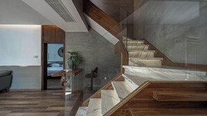 Um interior moderno com escada, vigas de madeira e guarda-corrimão de vidro.