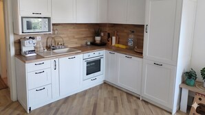 Moderni keittiö, jossa on valkoiset kaapit, puinen työtaso, sisäänrakennettu uuni ja mikroaaltouuni.