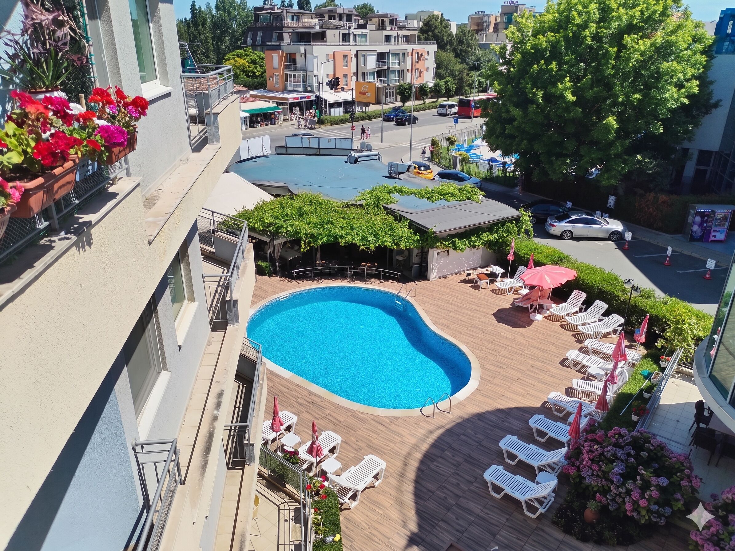 A rooftop pool with lounge chairs and umbrellas, surrounded by greenery and buildings.