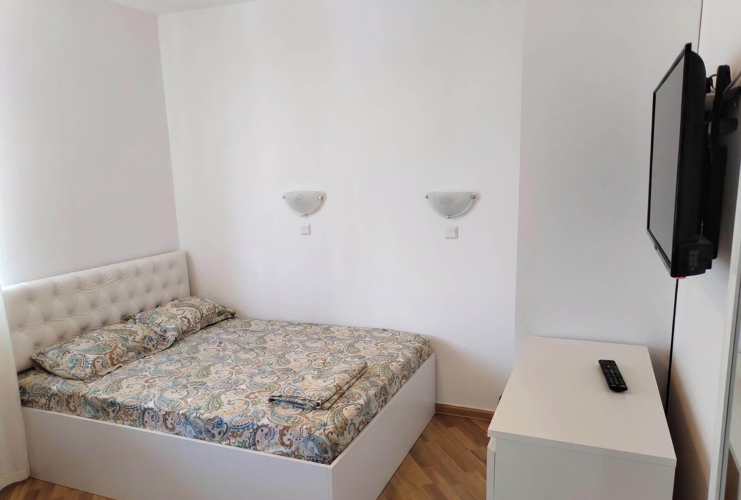 Quarto com cama, mesa de cabeceira, televisão e duas luzes na parede.